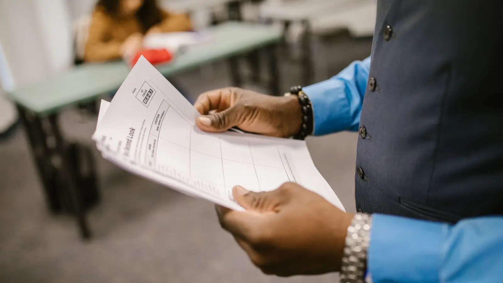 A teacher holding marked exam papers in a classroom, the kind of results sheet used to convert IB points into a German Abitur grade.