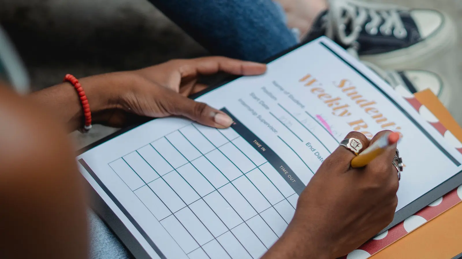 A student filling in a blank weekly timetable by hand, the first step in building a study schedule