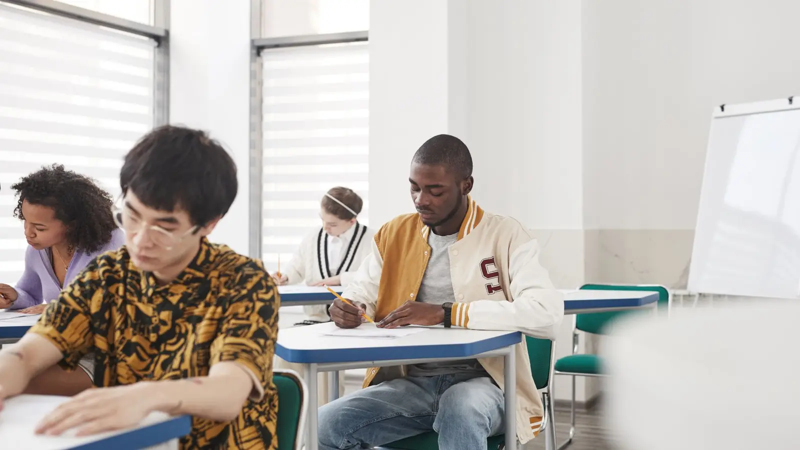 Secondary school students sitting at separate desks writing a final exam, the format used for the written papers of the German Abitur.